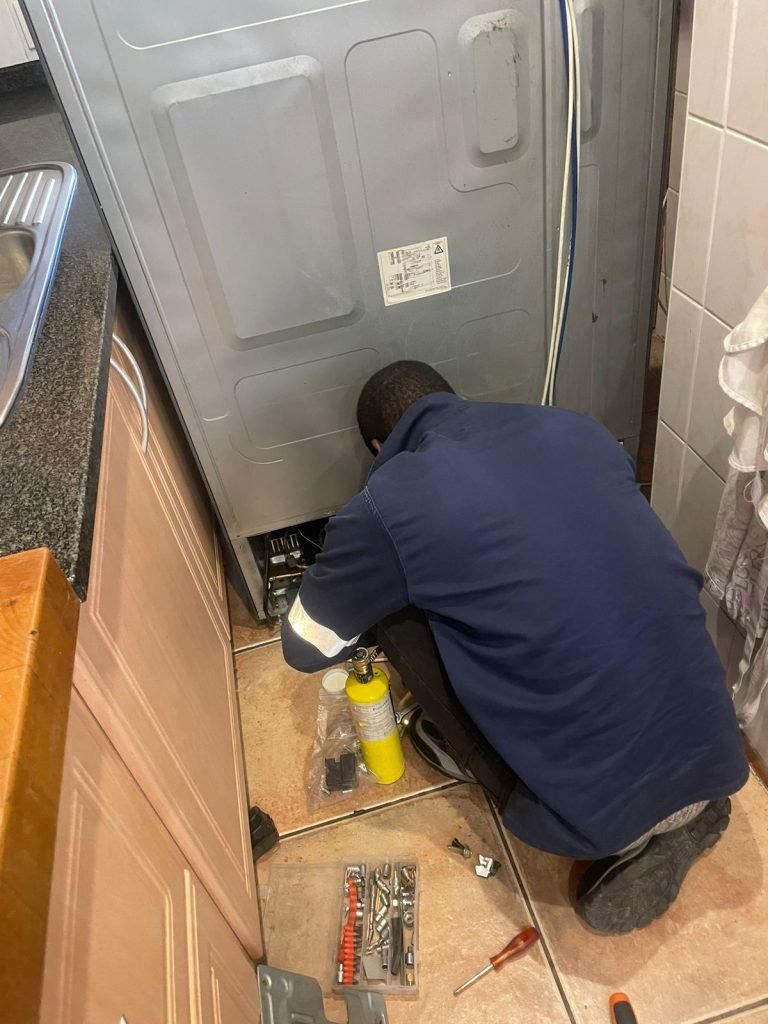 Expert technician checking the compressor unit at the back of a refrigerator in Riyadh